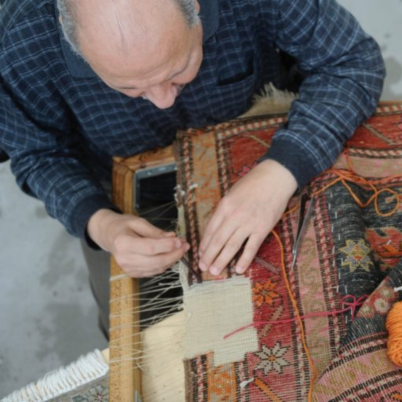 Carpet repair specialist carefully restoring a vintage rug with precision and skill.
