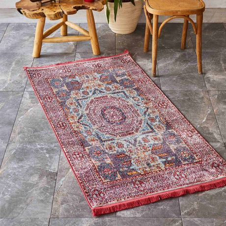 A small-sized vintage red rug with traditional motifs is laid out on a marble surface. Around the rug, there are wooden chairs placed at the edges, and a white planter sits nearby, adding a touch of contrast and elegance to the setting