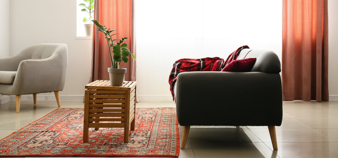 Red vintage Turkish rug with traditional patterns, featuring a wooden small table with a plant pot on top, and a black armchair with a red cover next to the table