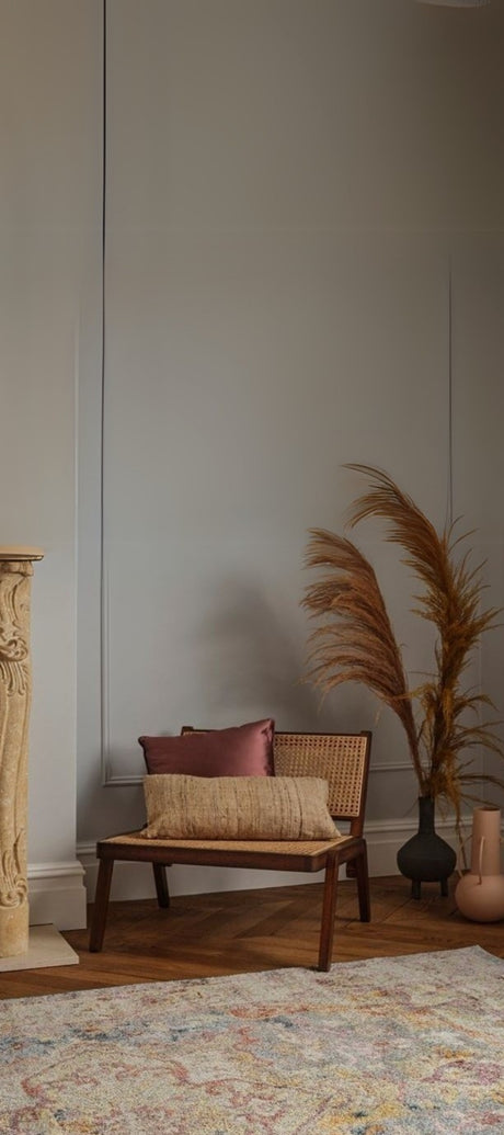 Vintage beige traditional patterned rug with red and beige pillows on a wooden chair, surrounded by plants in a pot and a vase, set against a clean white wall. Perfect for rustic, boho, and vintage home décor.