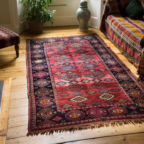 A vintage rug in red and black colors with traditional patterns, laid on the floor. The intricate design and texture create a warm, timeless atmosphere.