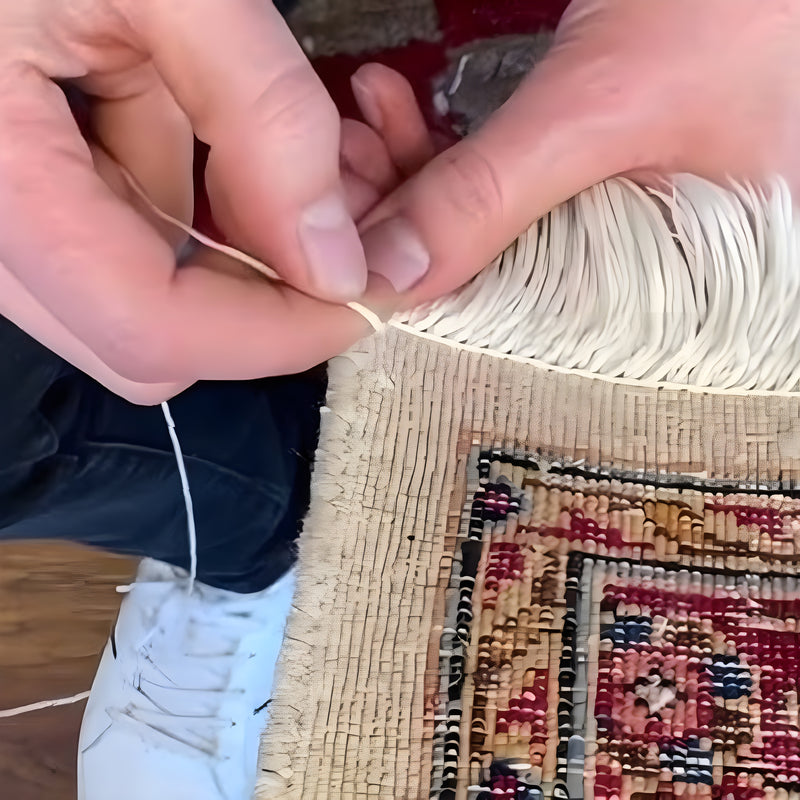 A person repairing the fringe of a vintage rug, carefully restoring its detail.